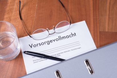 Dokument "Vorsorgevollmacht" mit Brille, Stift, Glas und Ordner auf einem Tisch.