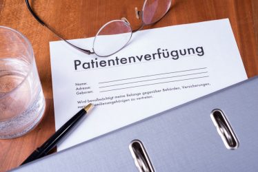 Patientenverfügung auf Tisch mit Glas, Brille, Stift und Ordner.