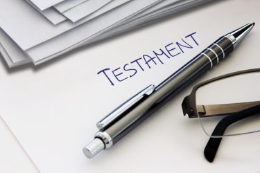 Dokument mit der Aufschrift "TESTAMENT", ein Stift und eine Brille liegen darauf.