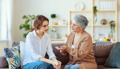 Zwei Frauen sitzen auf einem Sofa und führen ein Gespräch in einem Wohnzimmer.