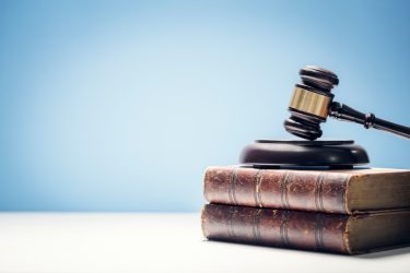 Richterhammer auf zwei alten Büchern vor blauem Hintergrund.