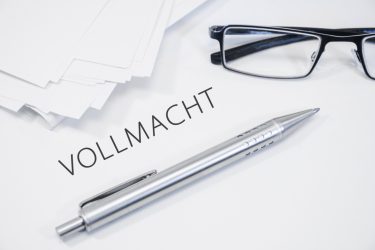 Dokumentstapel mit der Aufschrift "Vollmacht", Silberstift und schwarze Brille.