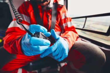 Eine Person trägt blaue Handschuhe und hält ein Funkgerät im Hubschrauber.