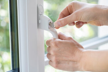 Hände schließen Fenster mit Schlüssel ab.