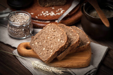 Dreifach geschnittenes Vollkornbrot mit Sonnenblumenkernen auf Holzbrett.