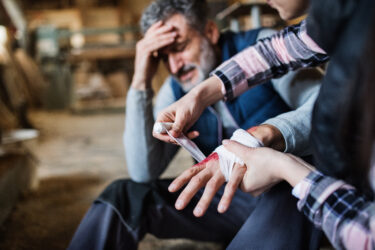 Eine Person verbindet die Hand einer anderen verletzten Person in einer Werkstattumgebung.