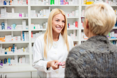 Eine Apothekerin berät eine Kundin in einer Apotheke. Regale mit Medikamenten im Hintergrund.
