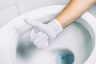Hand in weißem Handschuh zeigt Daumen hoch über einer Toilettenschüssel.
