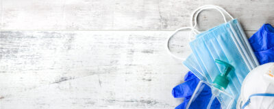 Blaue Masken, Handschuhe, Desinfektionsmittel und ein weißer Hintergrund.