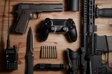 Ein Funkgerät, Messer, Patronen, Handfeuerwaffe, Spiele-Controller und Gewehr auf Holztisch.