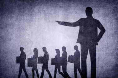 Schatten von Menschen mit Kartons gehen an großem Schatten einer zeigenden Person vorbei.