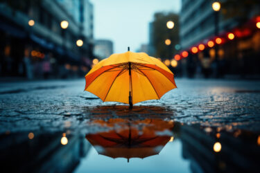 Ein gelber Regenschirm steht auf einer nassen Straße, spiegelt sich in einer Pfütze.
