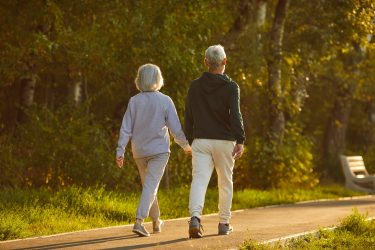 Senior couple in sportswear walking together on a path in a green park in summer